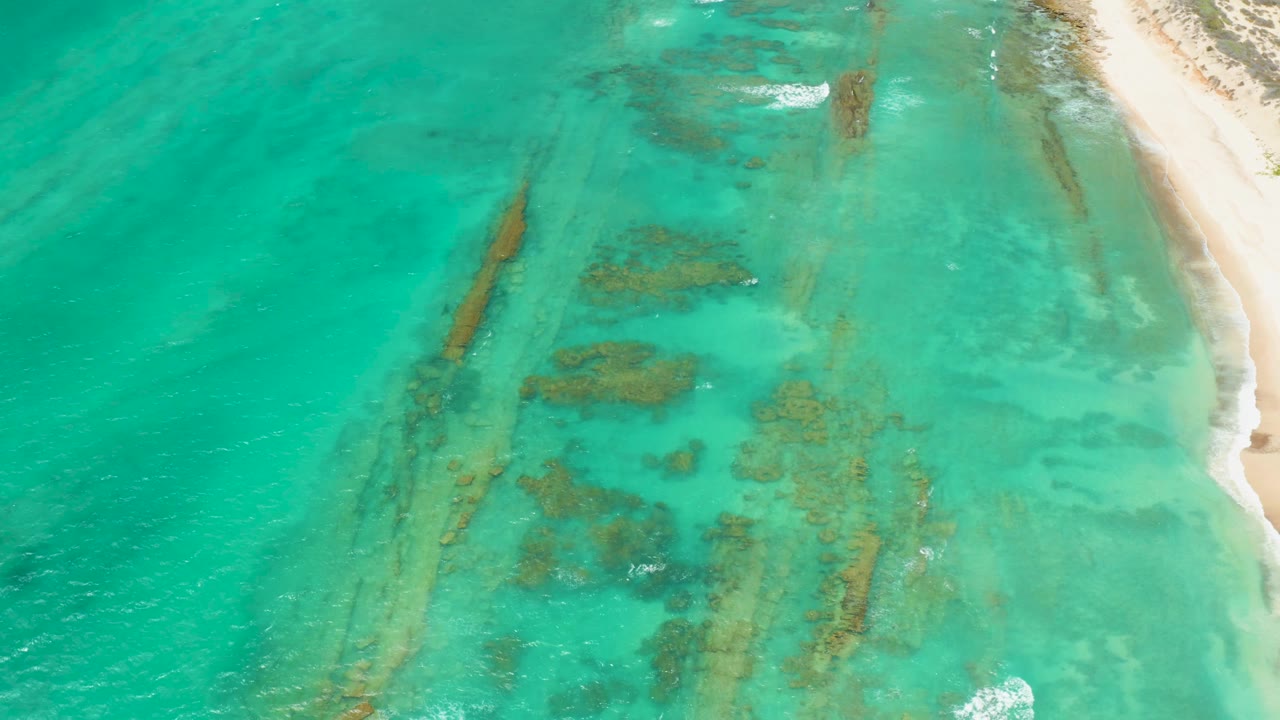 Turquoise coastal water with dark underwater formations and light foam near shore.