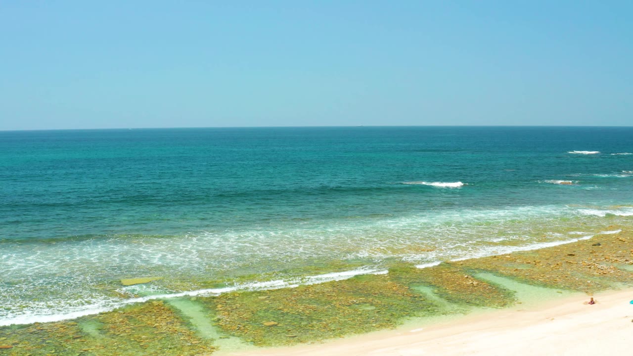 Aerial view of sandy beach, turquoise water, reef patches, and small surf lines.