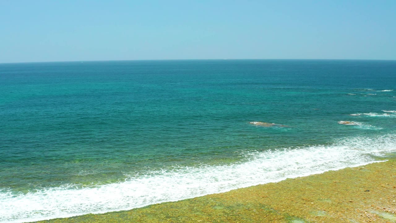 Turquoise ocean waves breaking over a shallow sandy shoreline.