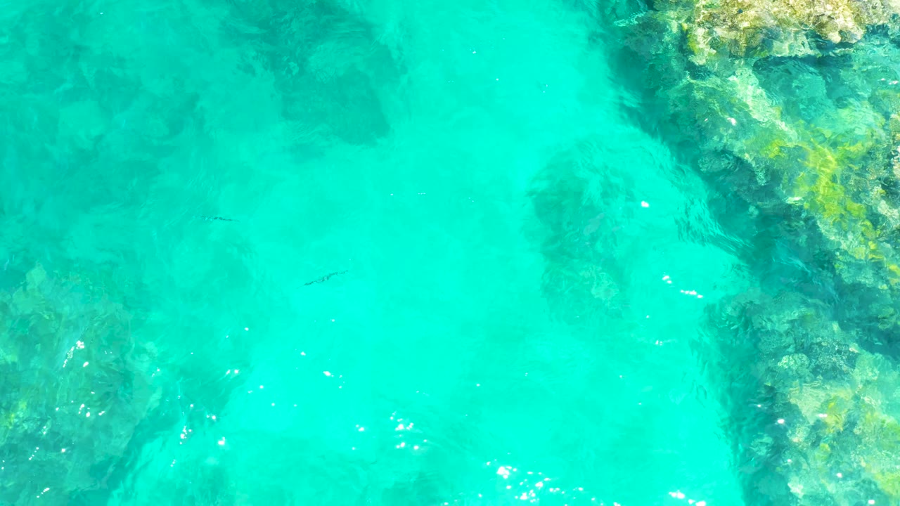 At 0:03, the El Tule Beach overhead frame shows small fish in clear turquoise water, darker submerged rock forms across the lower and right areas, and no visible people.