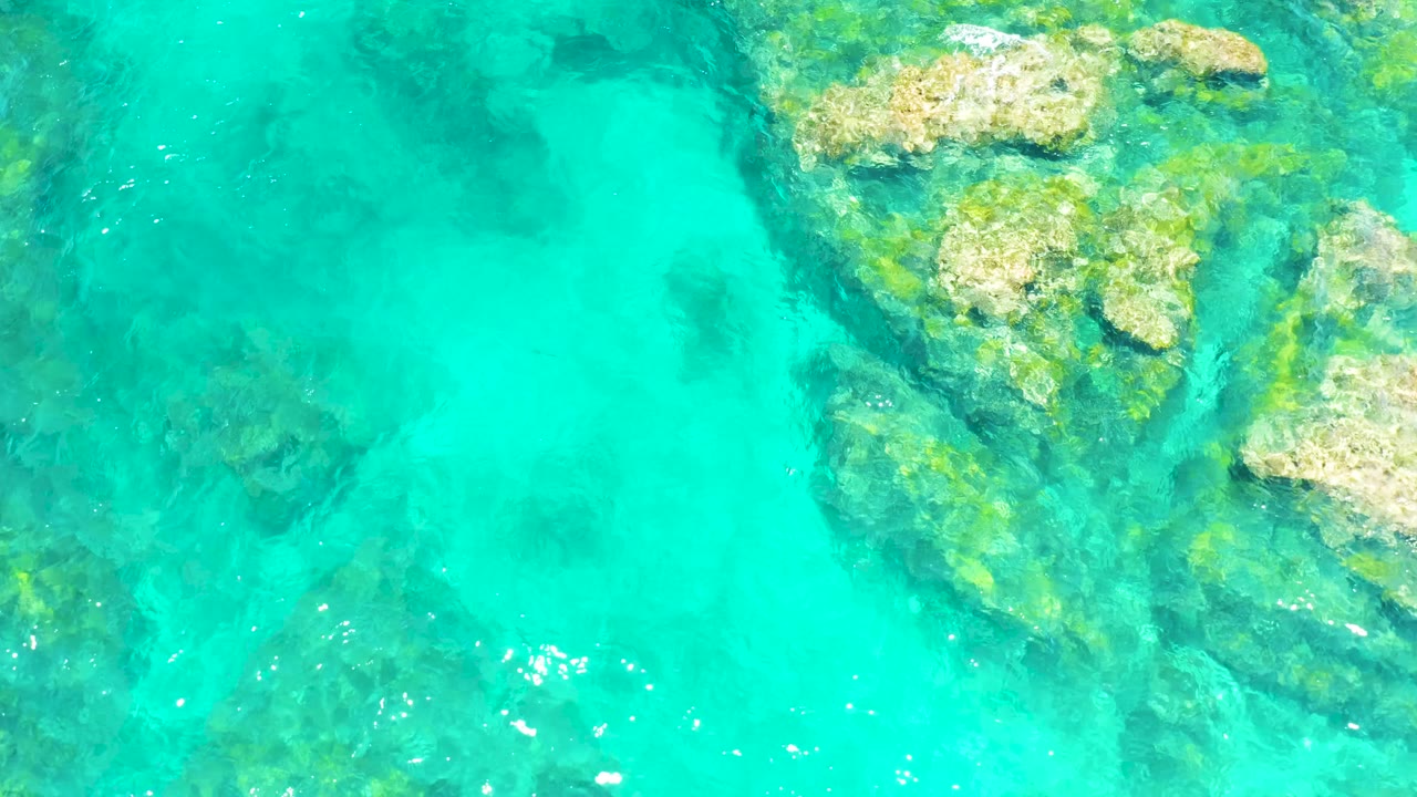 Bright turquoise water at El Tule Beach Los Cabos covers a large pale submerged rock formation along the right side, with no visible people.