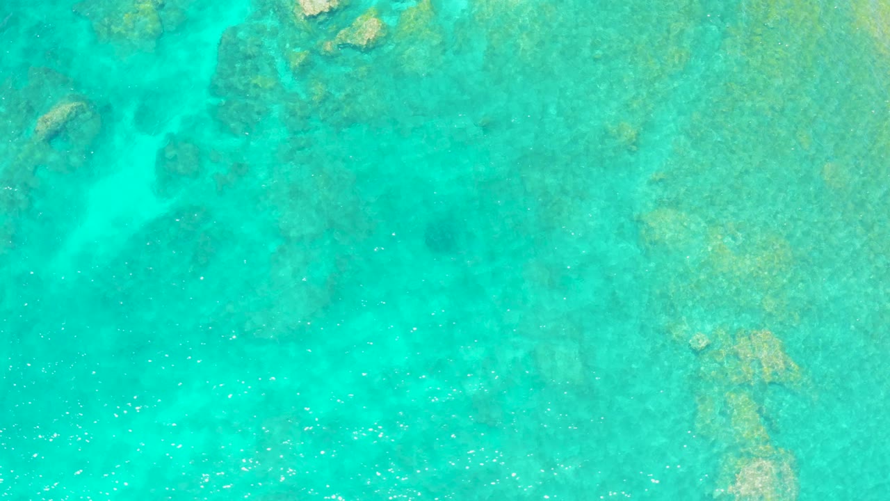 Clear green-blue ocean water reveals uneven reef texture below the surface at El Tule Beach Los Cabos, with small ripples moving across the frame and no visible people.