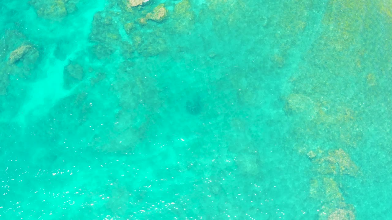Bright turquoise water covers mottled coral formations at El Tule Beach Los Cabos, with faint sparkle from ripples and no shoreline or visible people in frame.