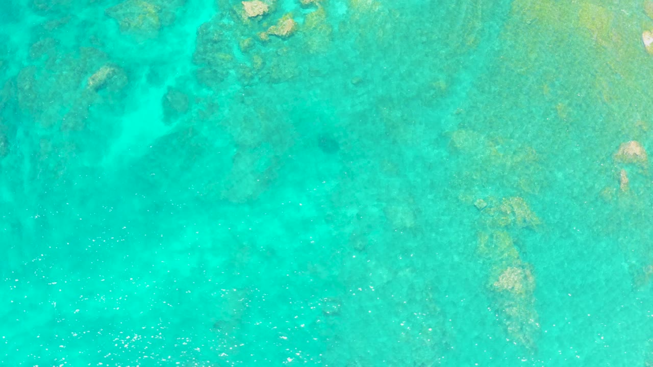 Clear turquoise water fills the frame at El Tule Beach Los Cabos, with pale seabed patches and darker submerged rocks visible, no visible people.