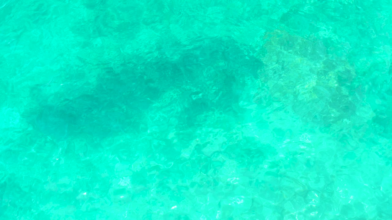 Overhead frame of clear turquoise ocean water at El Tule Beach Los Cabos, with pale seabed texture and darker submerged patches, no visible people.