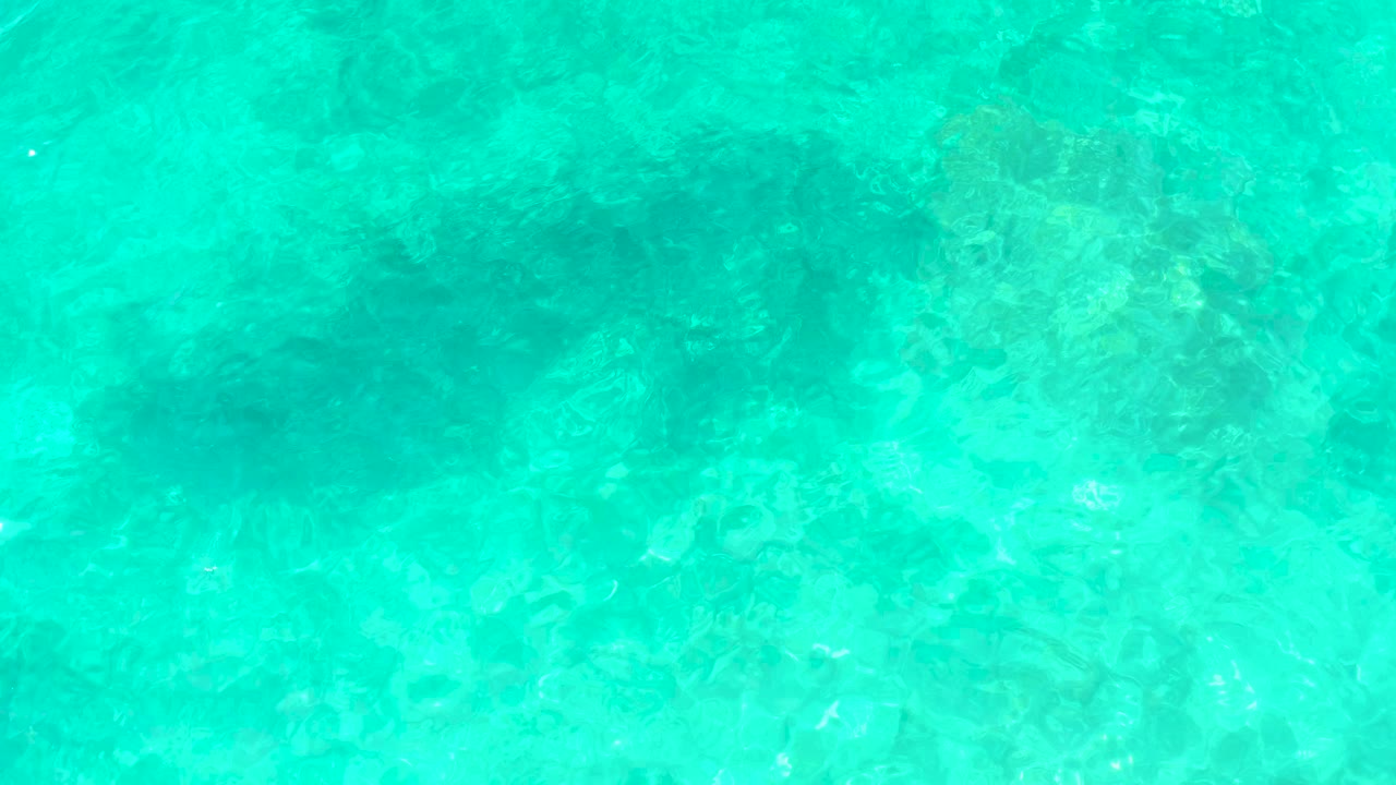 Clear aquamarine water at El Tule Beach Los Cabos shows darker underwater patches beneath a lightly rippled surface, no visible people.