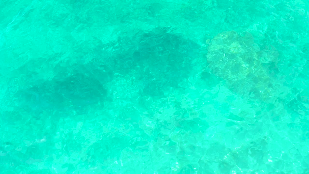 Turquoise ocean water at El Tule Beach Los Cabos reveals pale seabed detail with small bright reflections on the surface, no visible people.