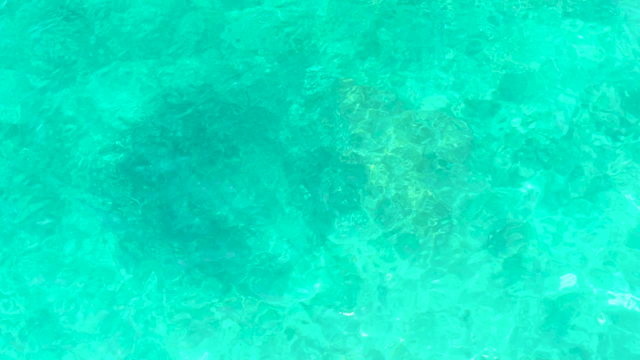 Turquoise shallow water at El Tule Beach in Los Cabos shows submerged rocks and soft surface ripples, with no visible people.
