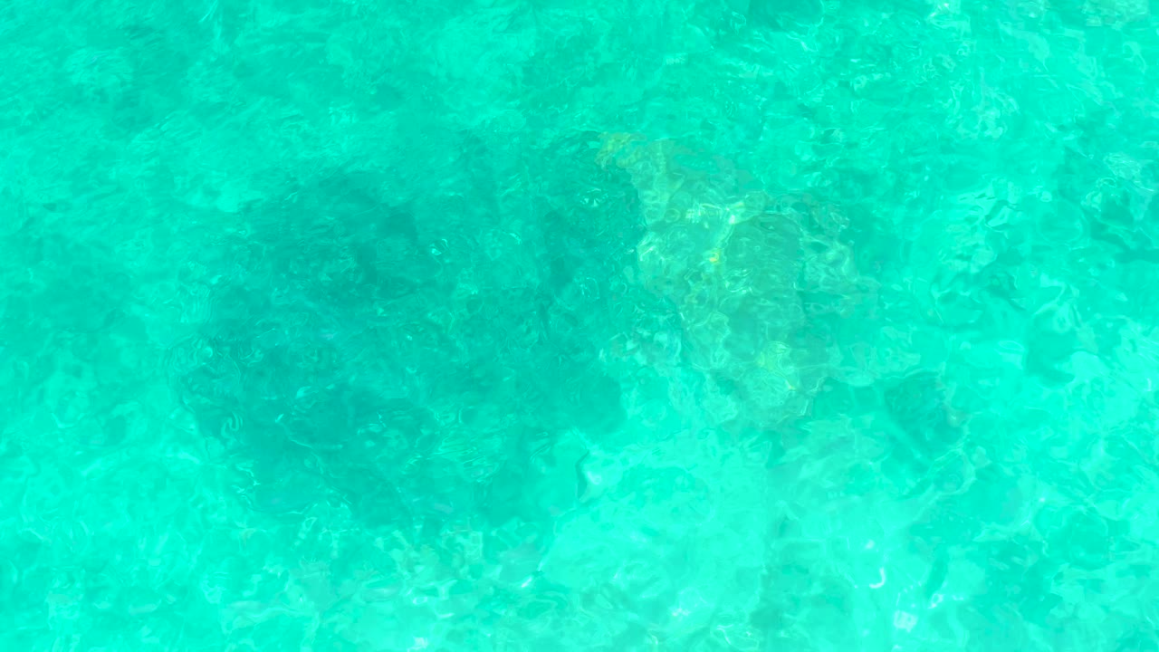 Shallow turquoise water at El Tule Beach in Los Cabos shows brighter light shimmer across the submerged rock texture, with no visible people.