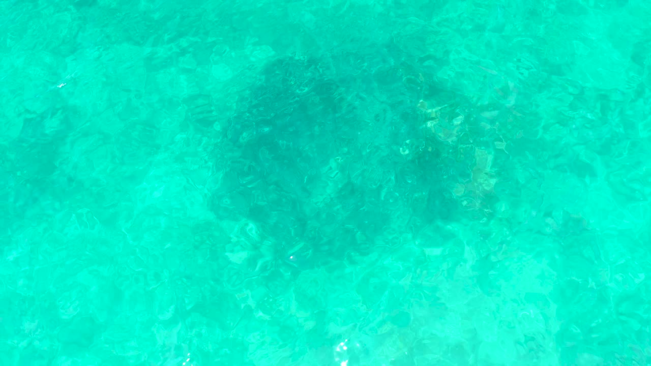 Bright turquoise water fills the frame at El Tule Beach in Los Cabos, with mottled seabed detail visible through the surface and no visible people.