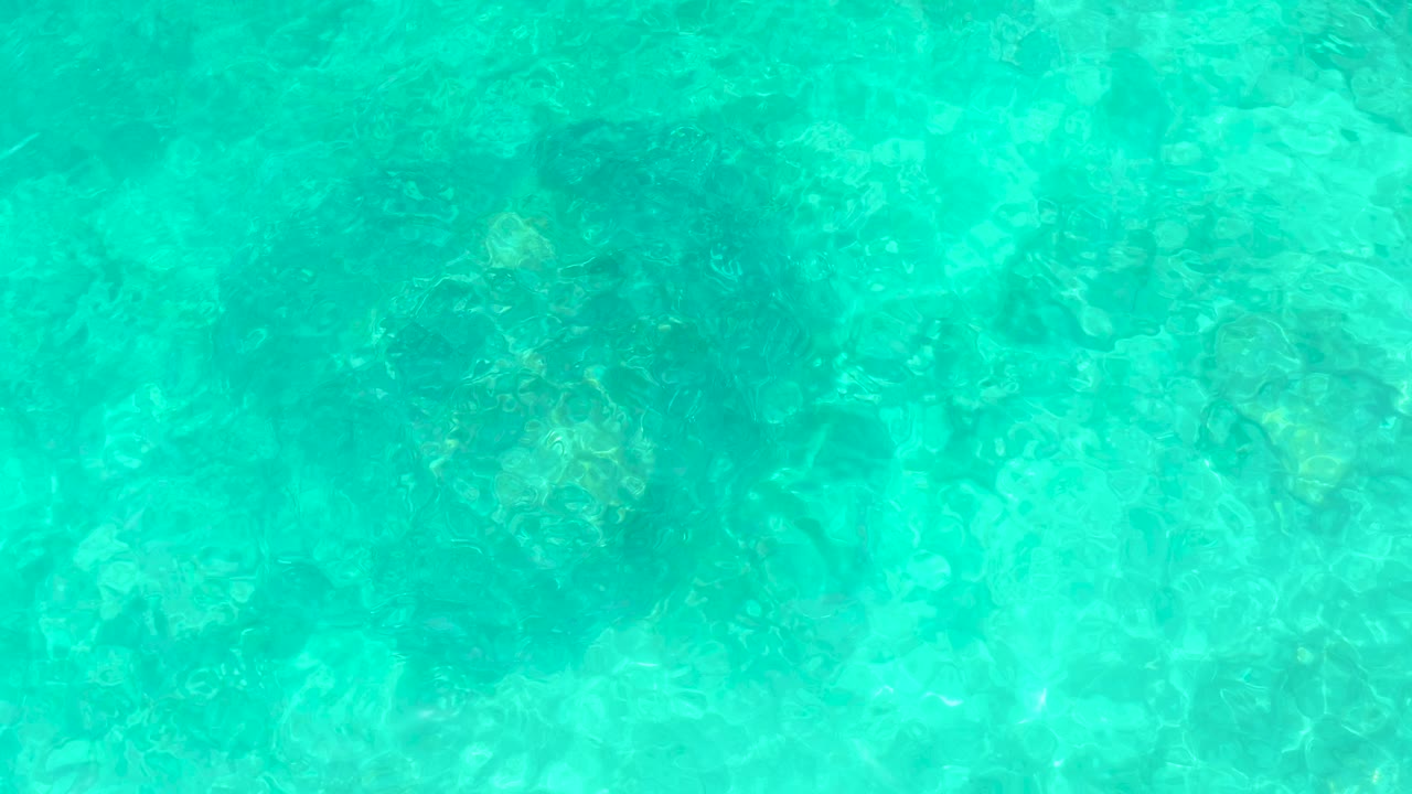Clear turquoise water at El Tule Beach Los Cabos shows pale seabed and darker underwater rock patches with no visible people.