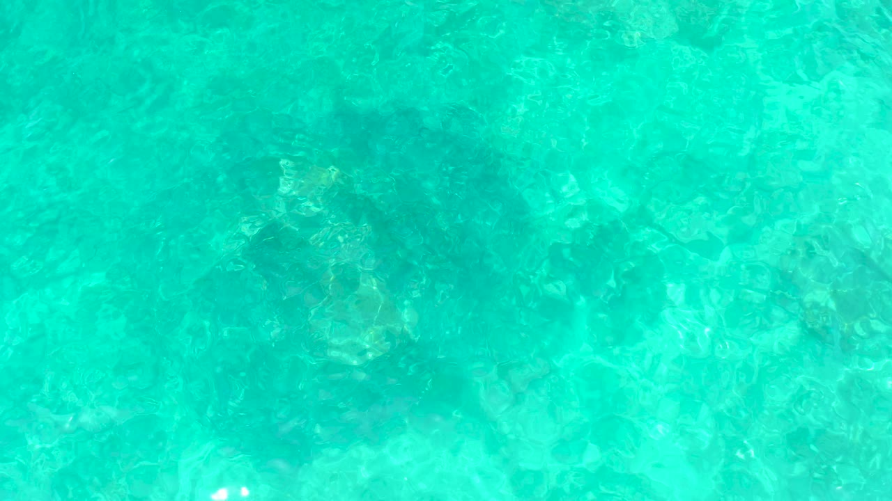 Turquoise ocean water at El Tule Beach Los Cabos reveals darker seabed patches beneath a lightly rippled surface, with no visible people.