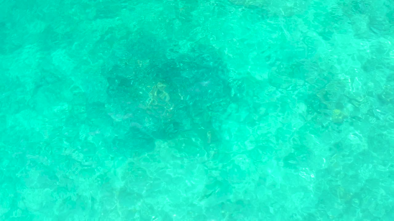 Clear turquoise water at El Tule Beach Los Cabos shows darker submerged patches under the rippled surface, with no visible people.