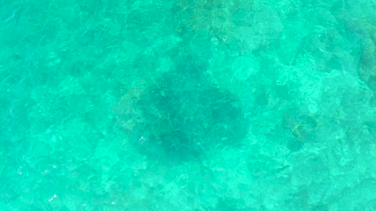 Top-down view of turquoise ocean water at El Tule Beach Los Cabos with dark submerged sinkhole shapes beneath ripples and no visible people.