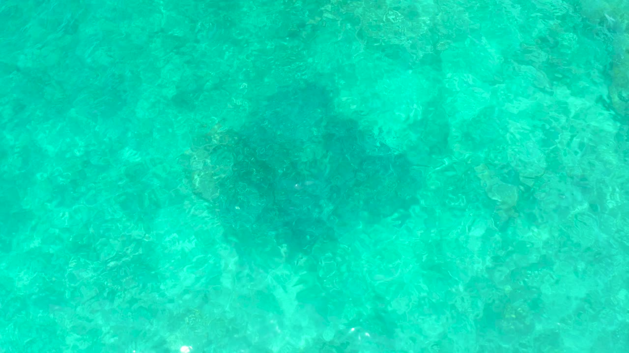 A top-down frame of El Tule Beach Los Cabos water shows turquoise surface ripples over a darker submerged sinkhole zone and no visible people.