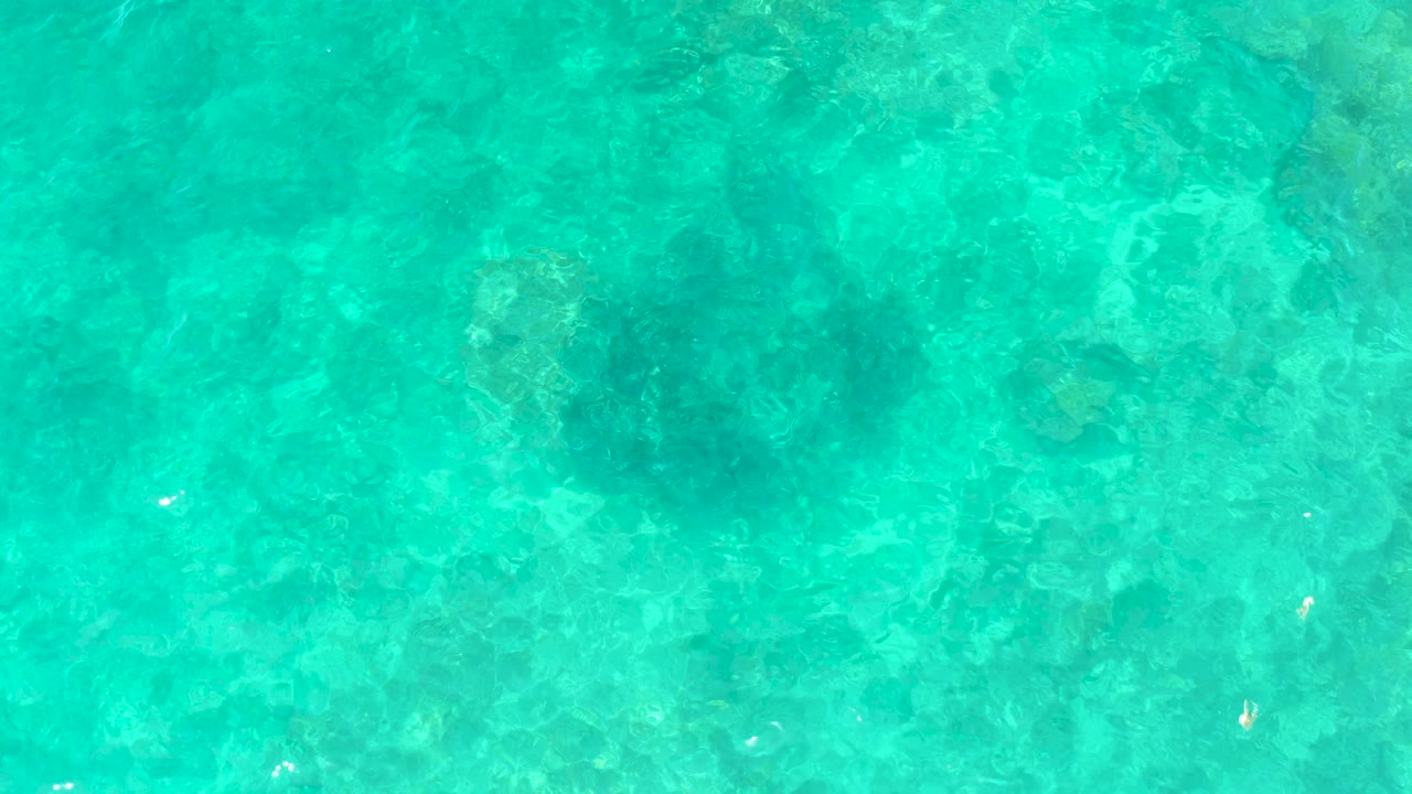 Overhead view of turquoise shallow water with darker seabed patches.