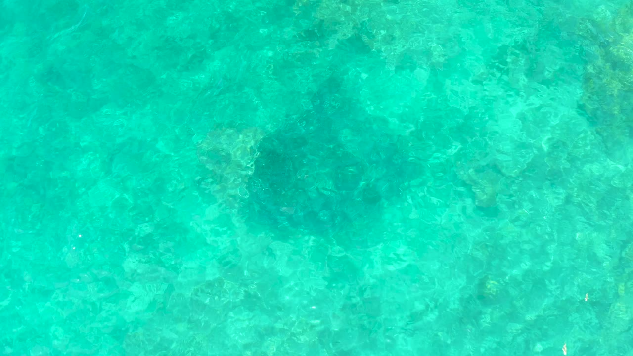 At 0:03, clear water at El Tule Beach Los Cabos fills the frame, with darker underwater areas softened by ripples and no visible people or shoreline.