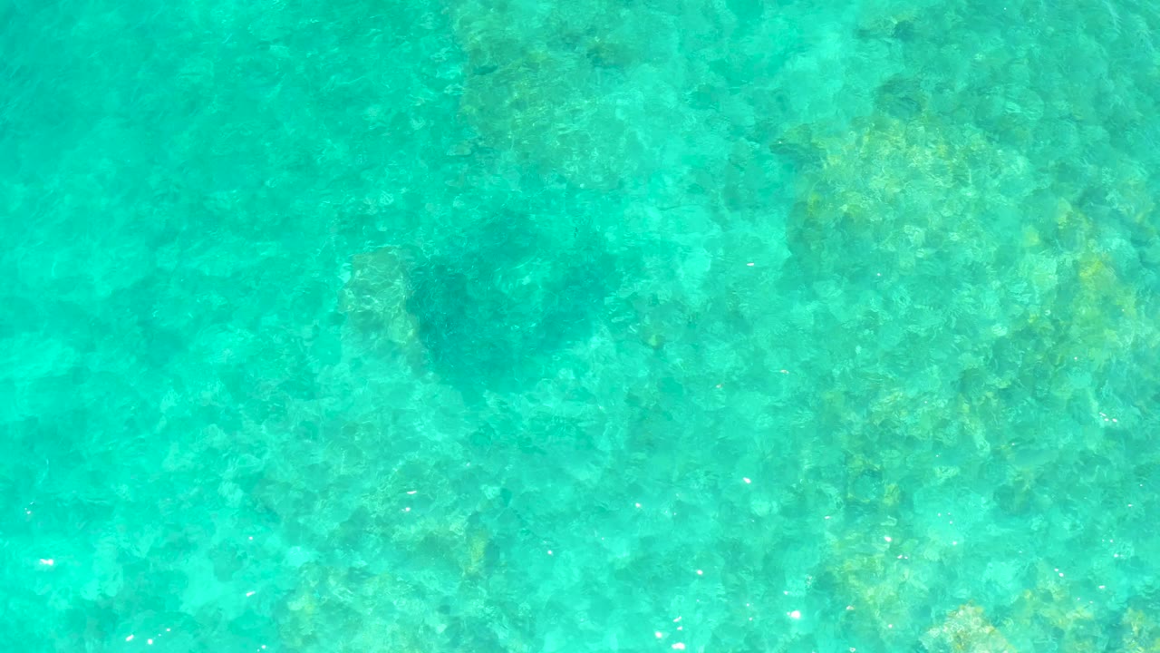 Clear shallow ocean water in El Tule Beach Los Cabos shows pale and dark seabed patches beneath soft surface ripples, with no visible people.