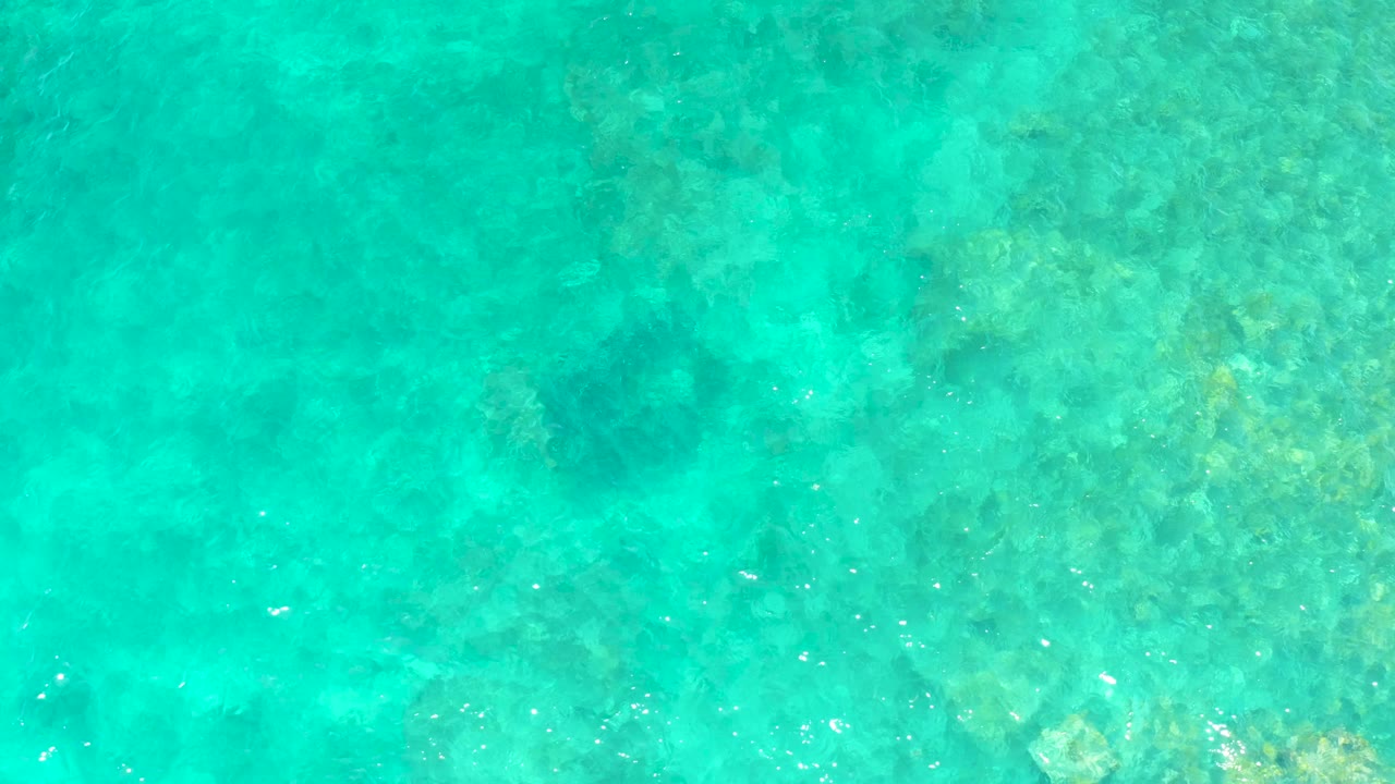 Transparent turquoise water exposes darker reef areas and lighter sandy-looking patches at El Tule Beach Los Cabos, with no visible people.