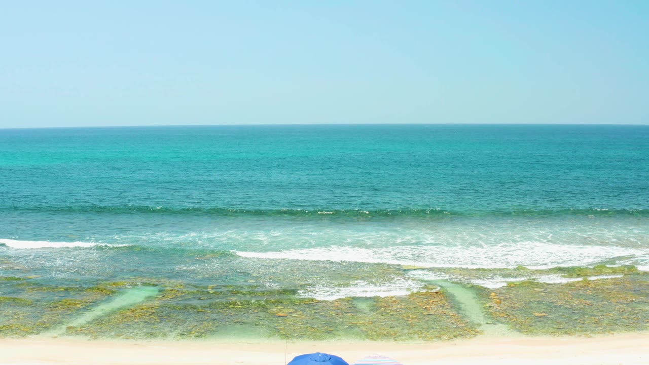Beach shoreline with waves and partial umbrellas near the lower edge