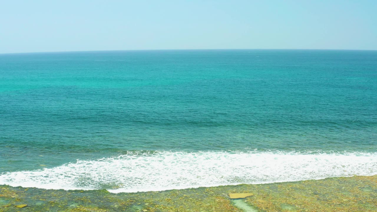 At 0:01, El Tule Beach Los Cabos shows a wider band of white foam pushing over shallow rocky reef, with open turquoise water behind it and no visible people.