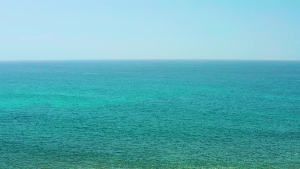 Aerial view of turquoise ocean at El Tule Beach Los Cabos with a level horizon, pale clear sky, and no visible people.