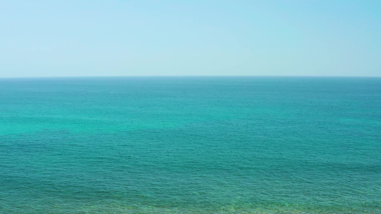 Open turquoise sea at El Tule Beach Los Cabos stretches to a straight horizon under light blue sky, with no shoreline or people visible.
