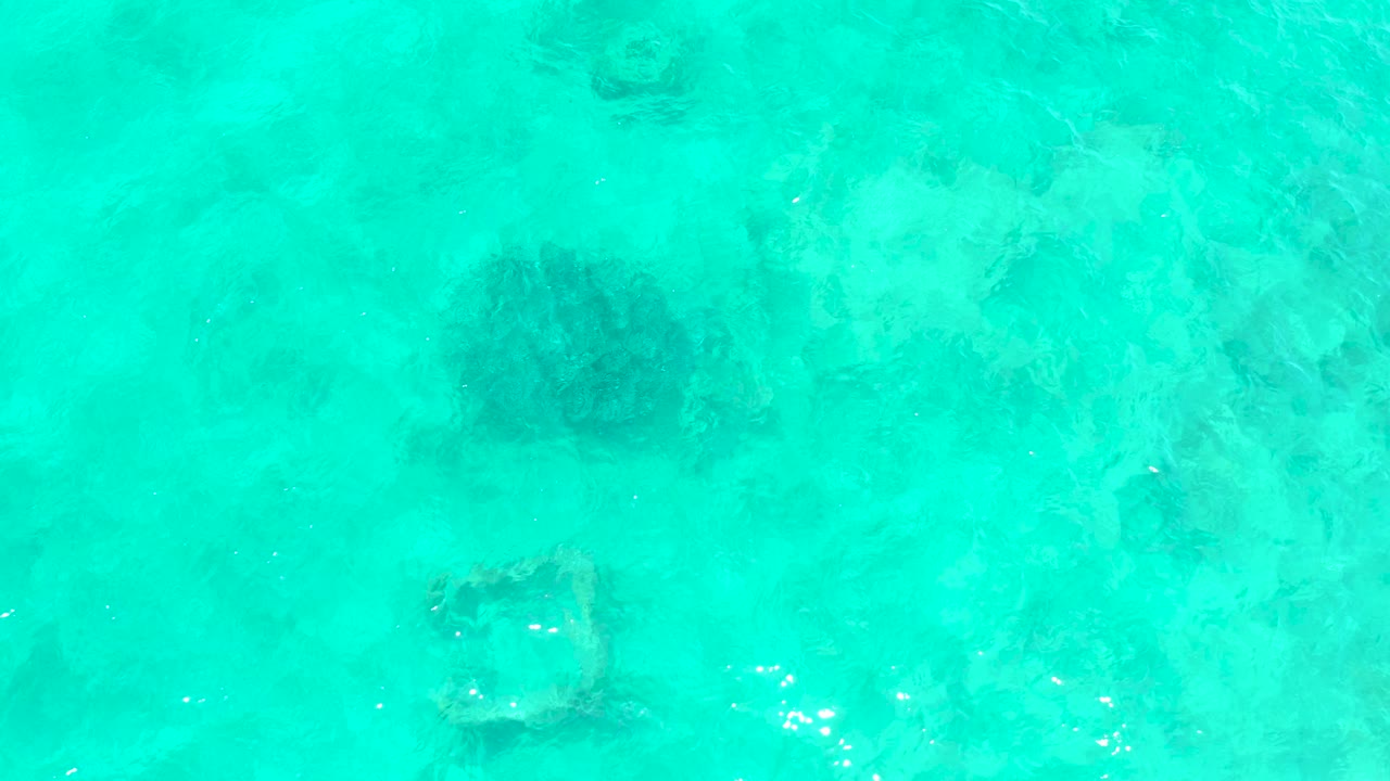 Turquoise shallow water with a dark rounded underwater formation and square submerged frame.