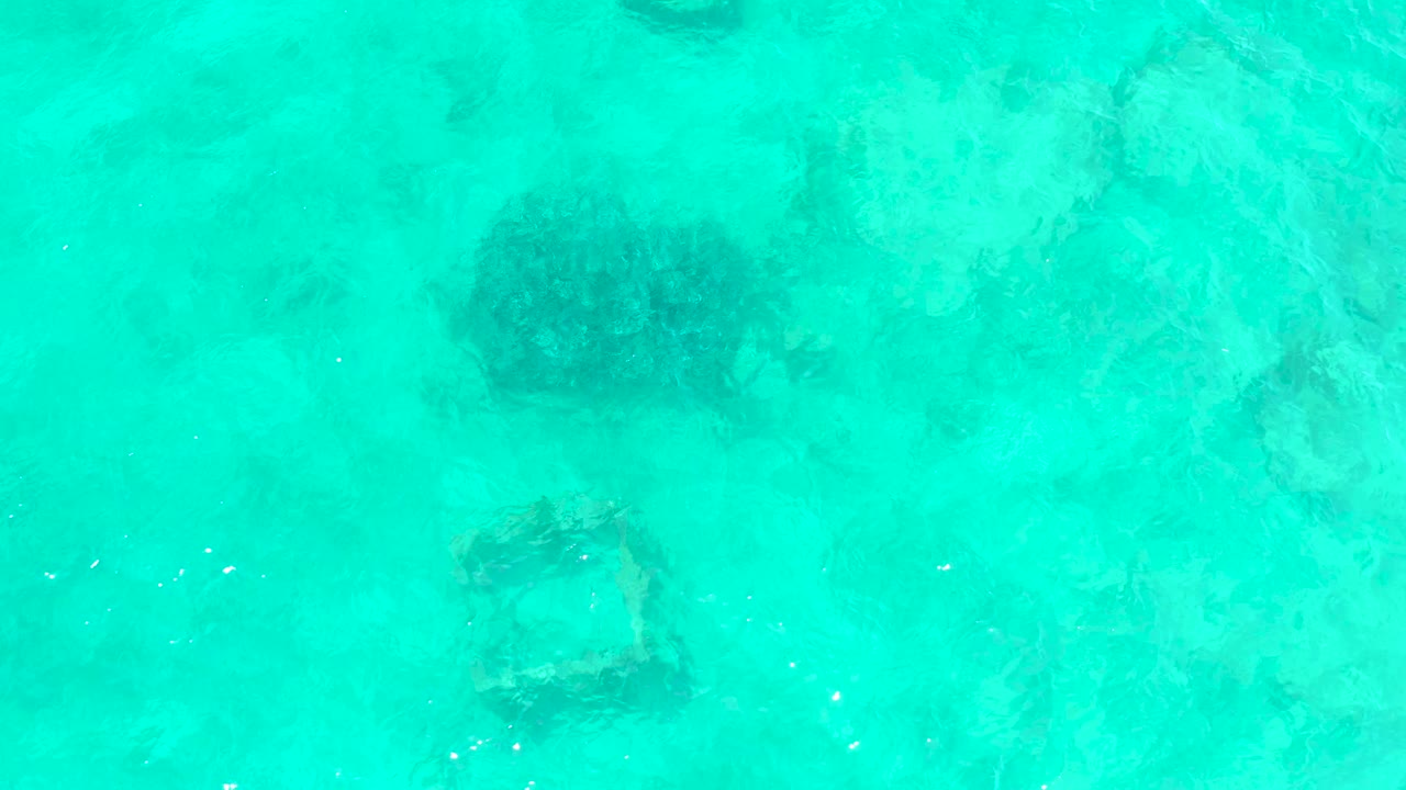 A darker rounded underwater patch and a square frame are seen through turquoise shallows at El Tule Beach Los Cabos, with ripples slightly softening the edges and no visible people.