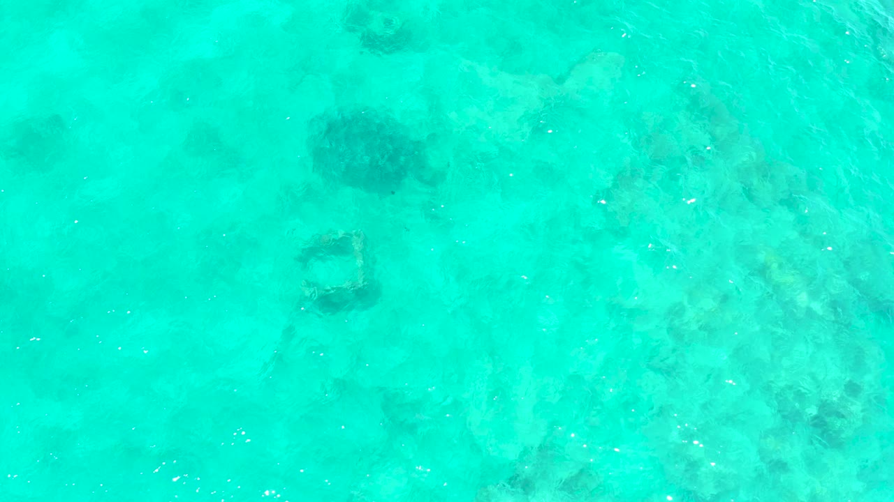 Top-down turquoise water with pale seabed and darker marine patches.