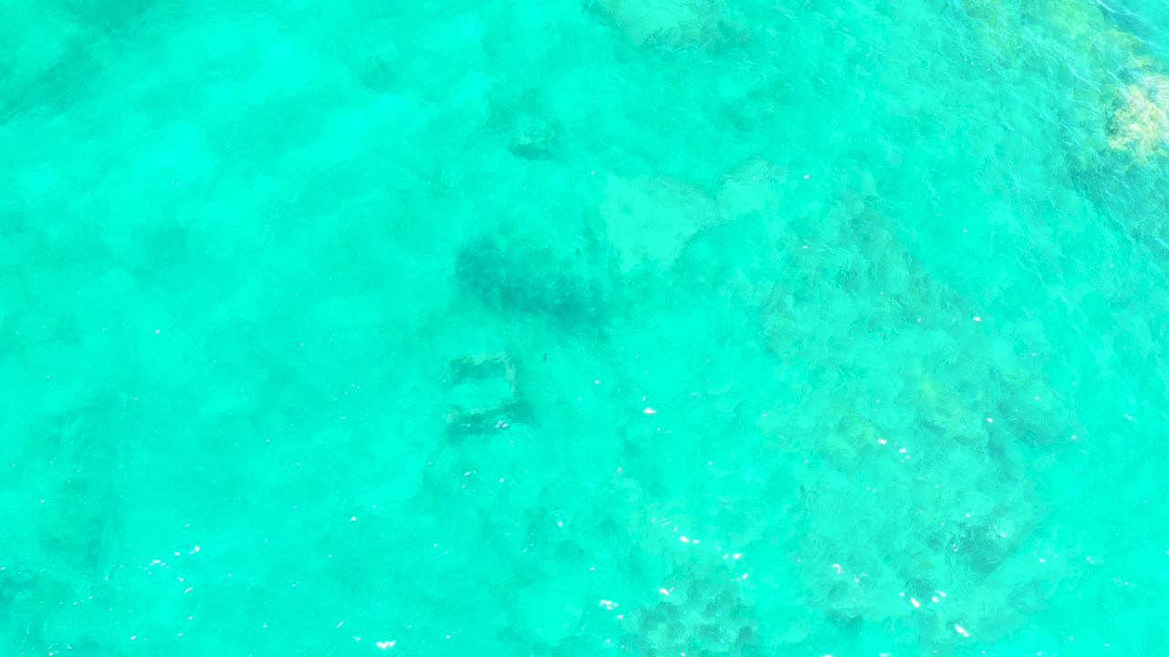 Clear aqua water at El Tule Beach, Los Cabos, shows darker submerged formations slightly shifted under rippled surface light, with no visible people.