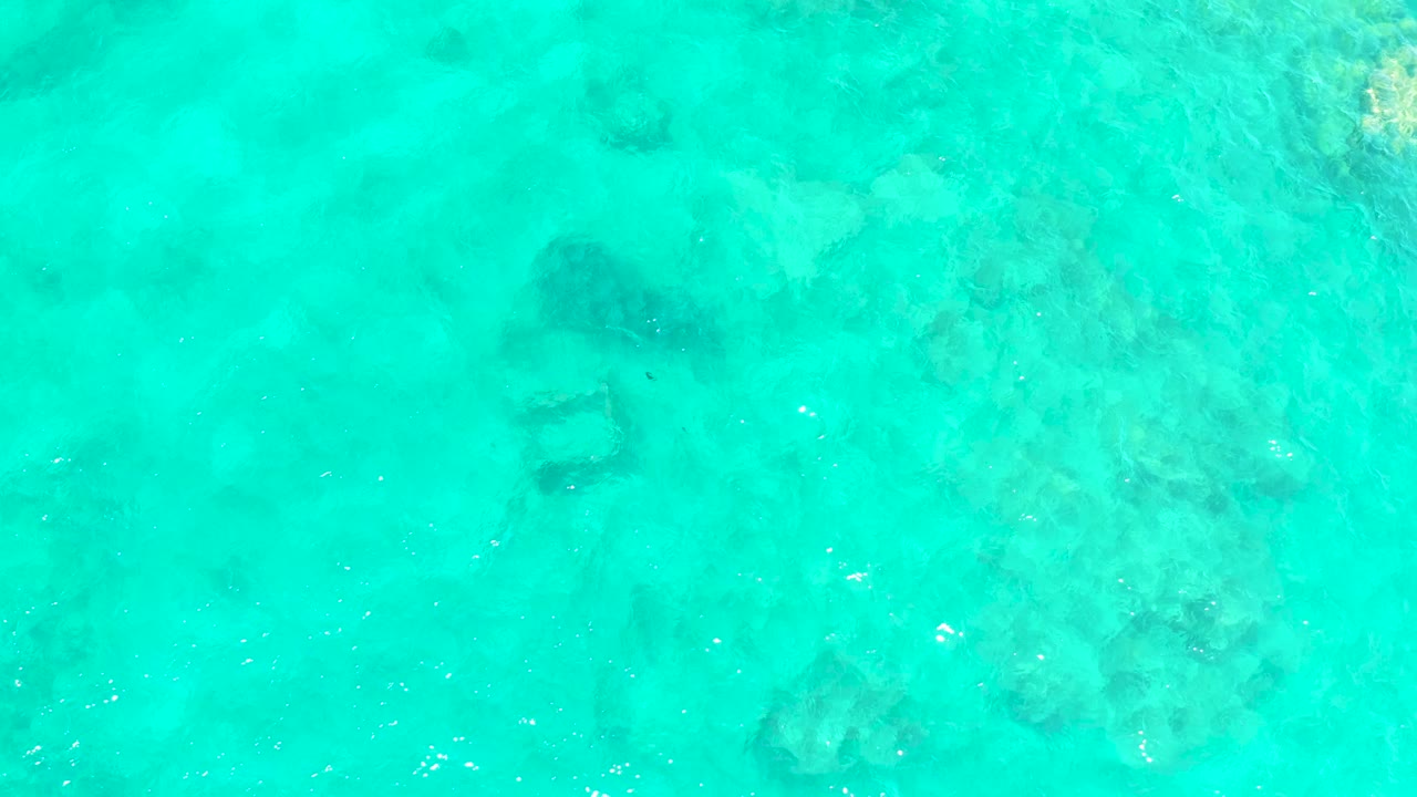 Bright turquoise water with ripples and submerged rocks.