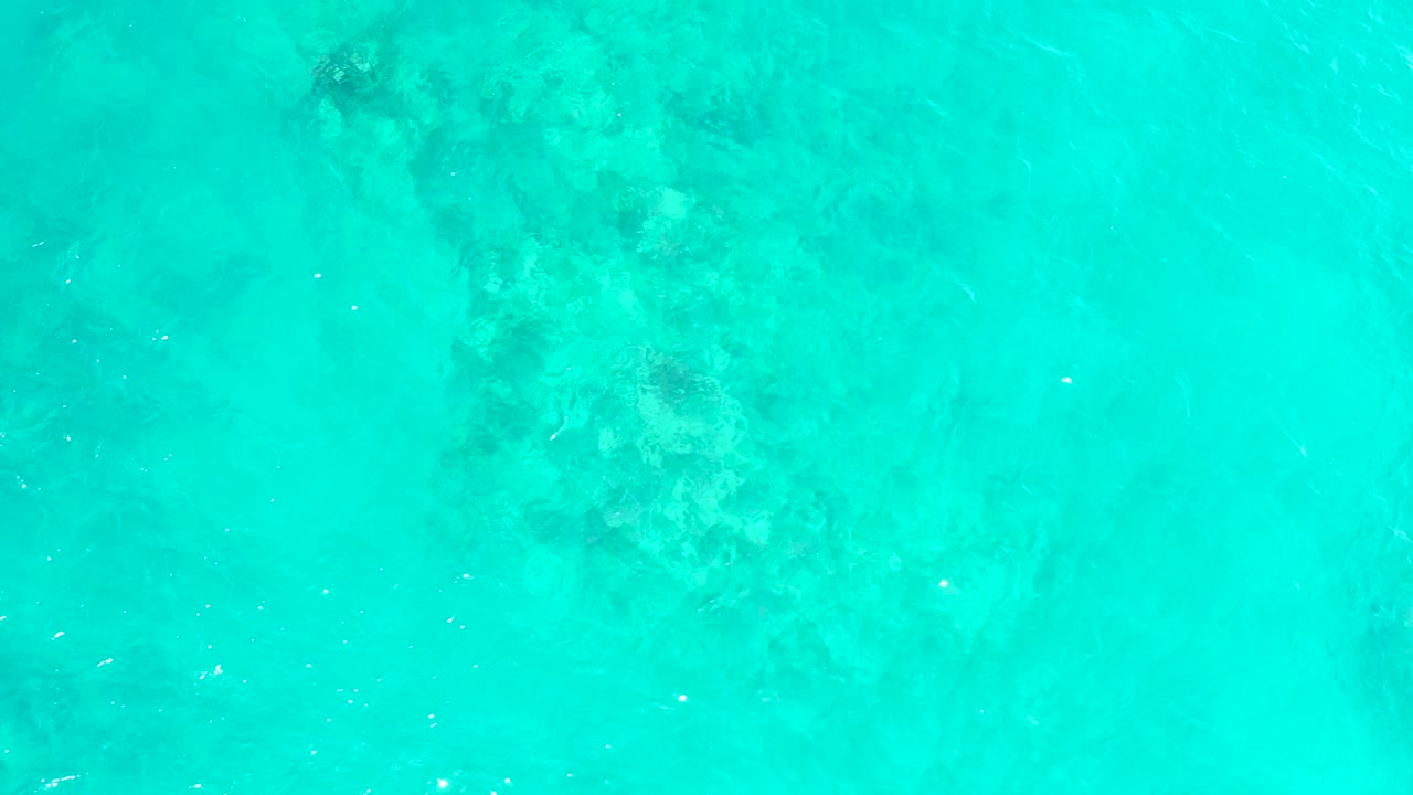 Clear turquoise water at El Tule Beach Los Cabos shows a mottled underwater coral and rock area centered high in the frame, with faint ripples and no visible people.
