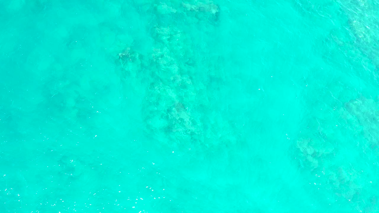 Clear shallow ocean water at El Tule Beach in Los Cabos shows a broad darker seabed area near the top center with fine ripples across the surface and no visible people.