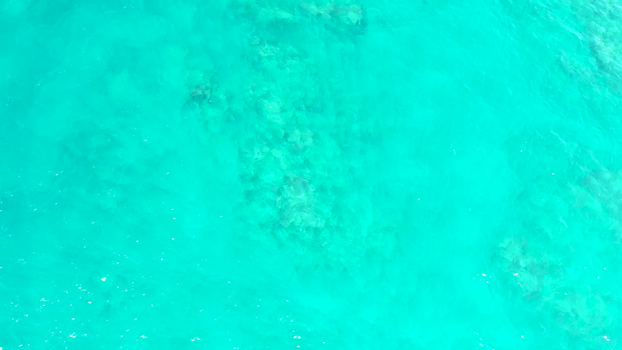A bright overhead water frame from El Tule Beach in Los Cabos shows faint mottled seabed patterns under turquoise water, with no shoreline or visible people.