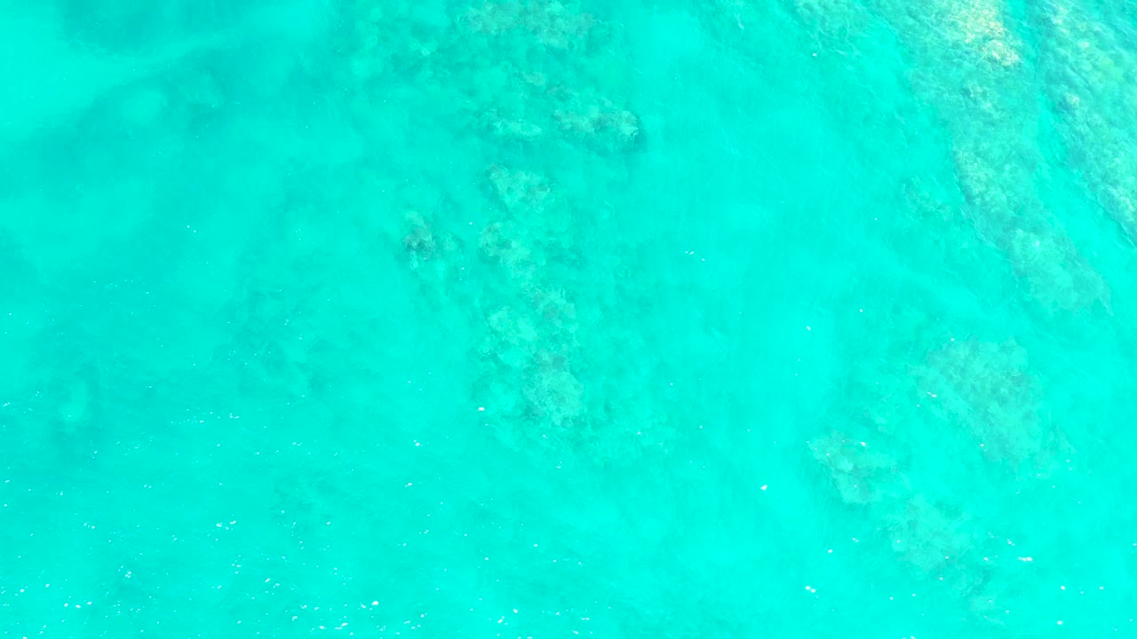 Clear turquoise ocean at El Tule Beach Los Cabos shows darker reef-like seabed shapes drifting across the upper and center areas, with no visible people.