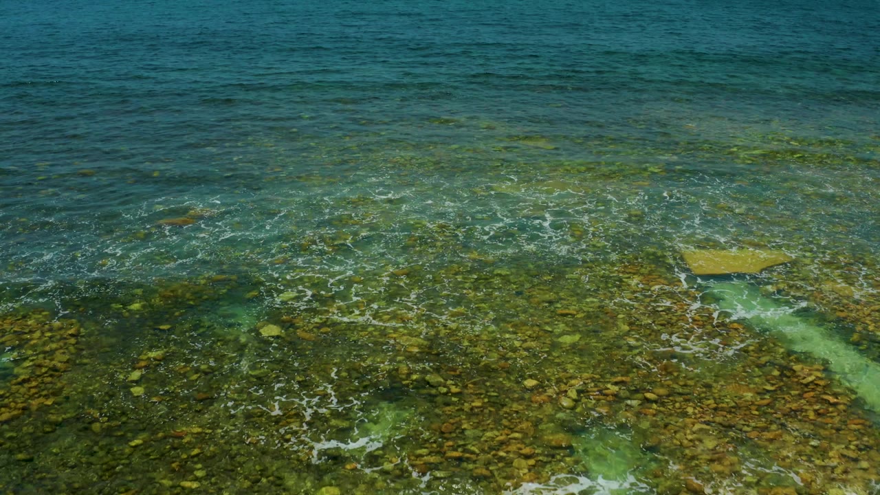 Clear coastal water over rocks with a pale turquoise channel and low foam.