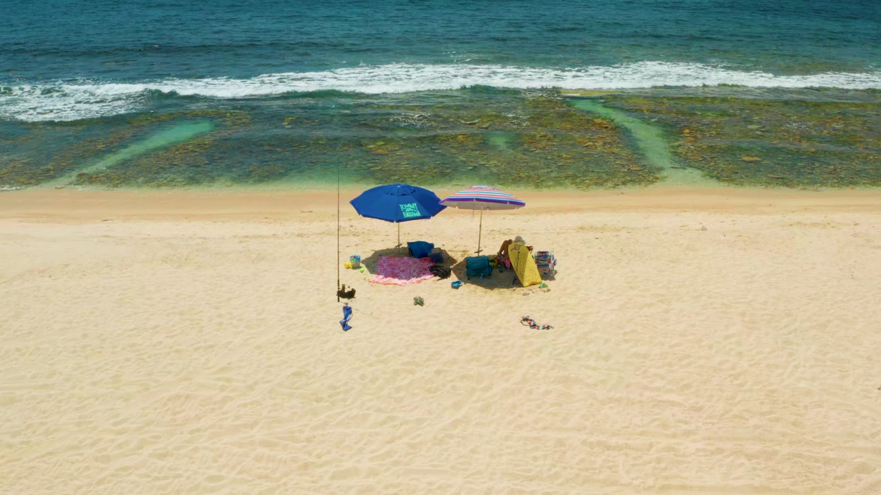 Overhead beach umbrellas on sand beside shallow ocean water.
