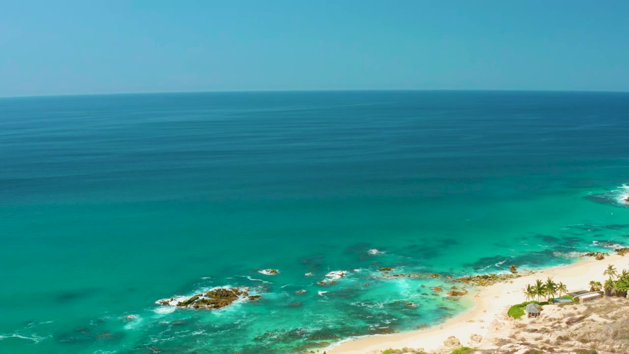 One second into the Dreams Los Cabos clip, the reef and foamy waves sit lower in frame beneath a wide band of deep blue ocean, with no visible people.