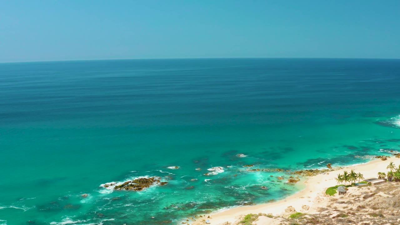 Wide elevated ocean view with surf breaking over rocks near a sandy beach.