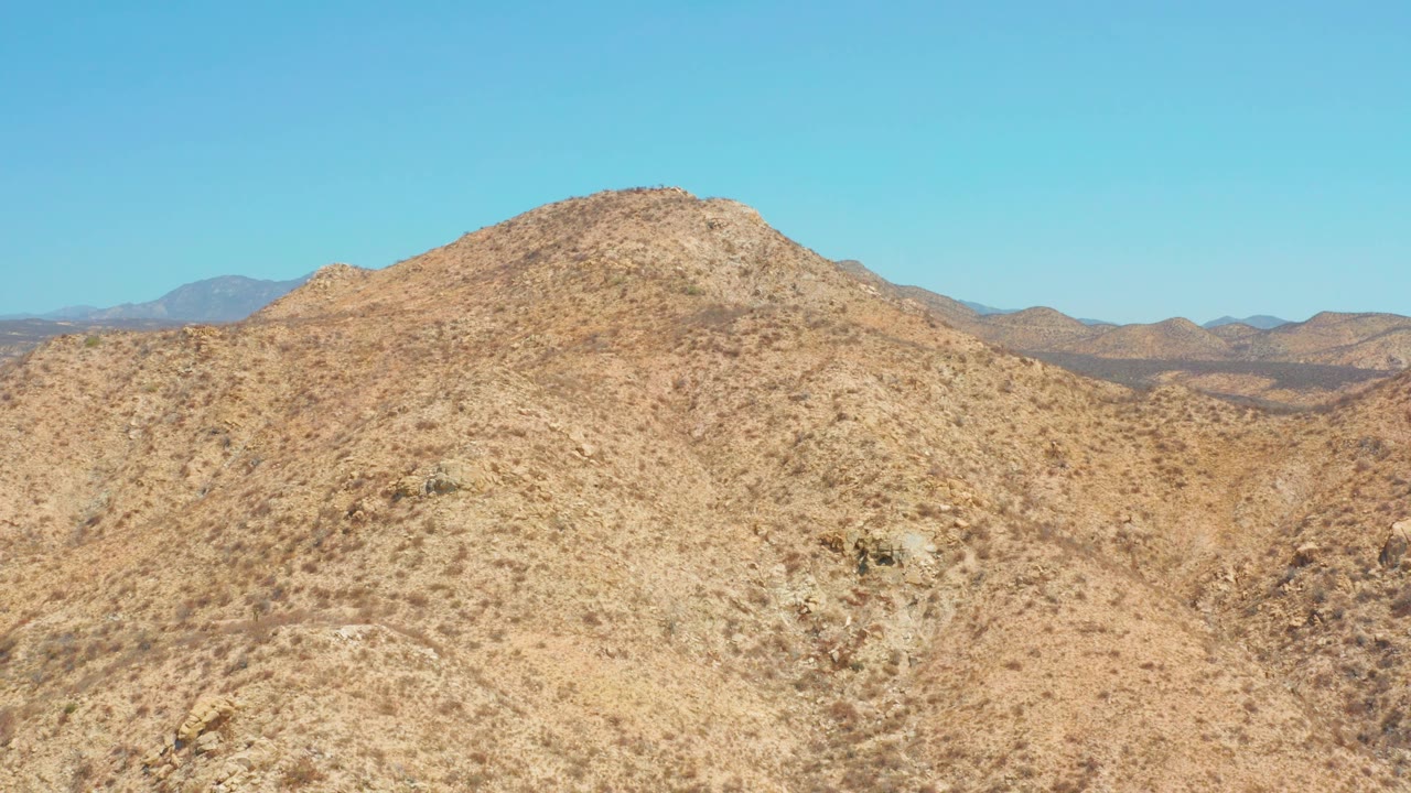 Slightly later view of the same arid hill near Dreams Los Cabos, with scrub-dotted slopes, darker rock patches, distant ridges, and no visible people.