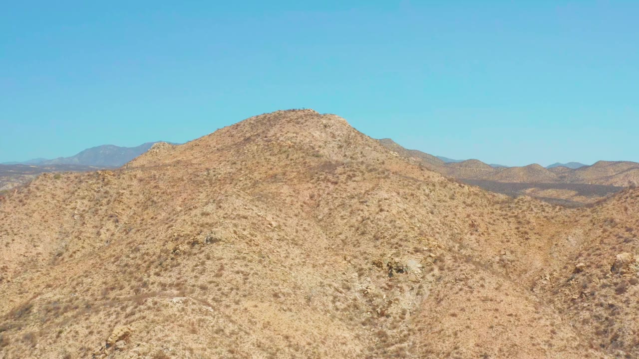 Second frame shows a rocky arid hillside near Dreams Los Cabos with patchy vegetation, pale tan ground, background mountains, and no visible people.