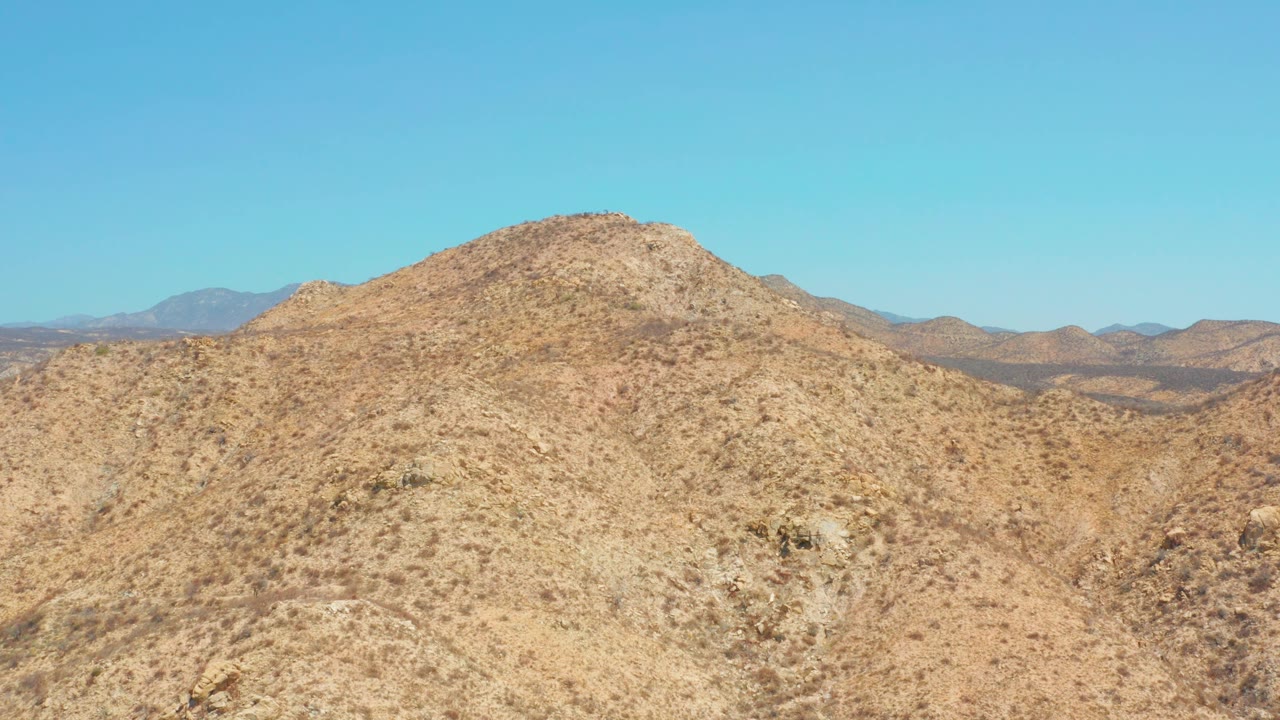 Fourth frame presents a wide desert hillside near Dreams Los Cabos with tan soil, sparse vegetation, distant ridgelines, and no visible people.