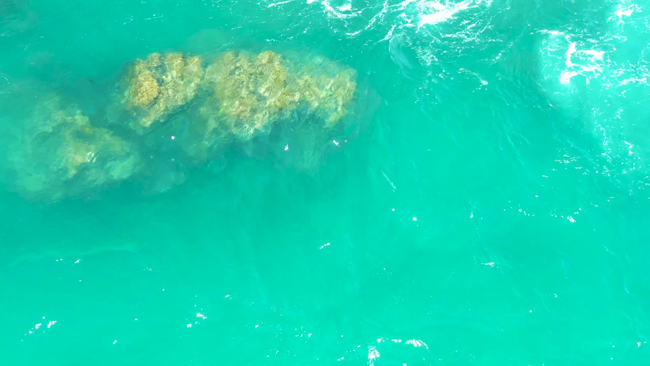 Large submerged rocks in shallow turquoise ocean water
