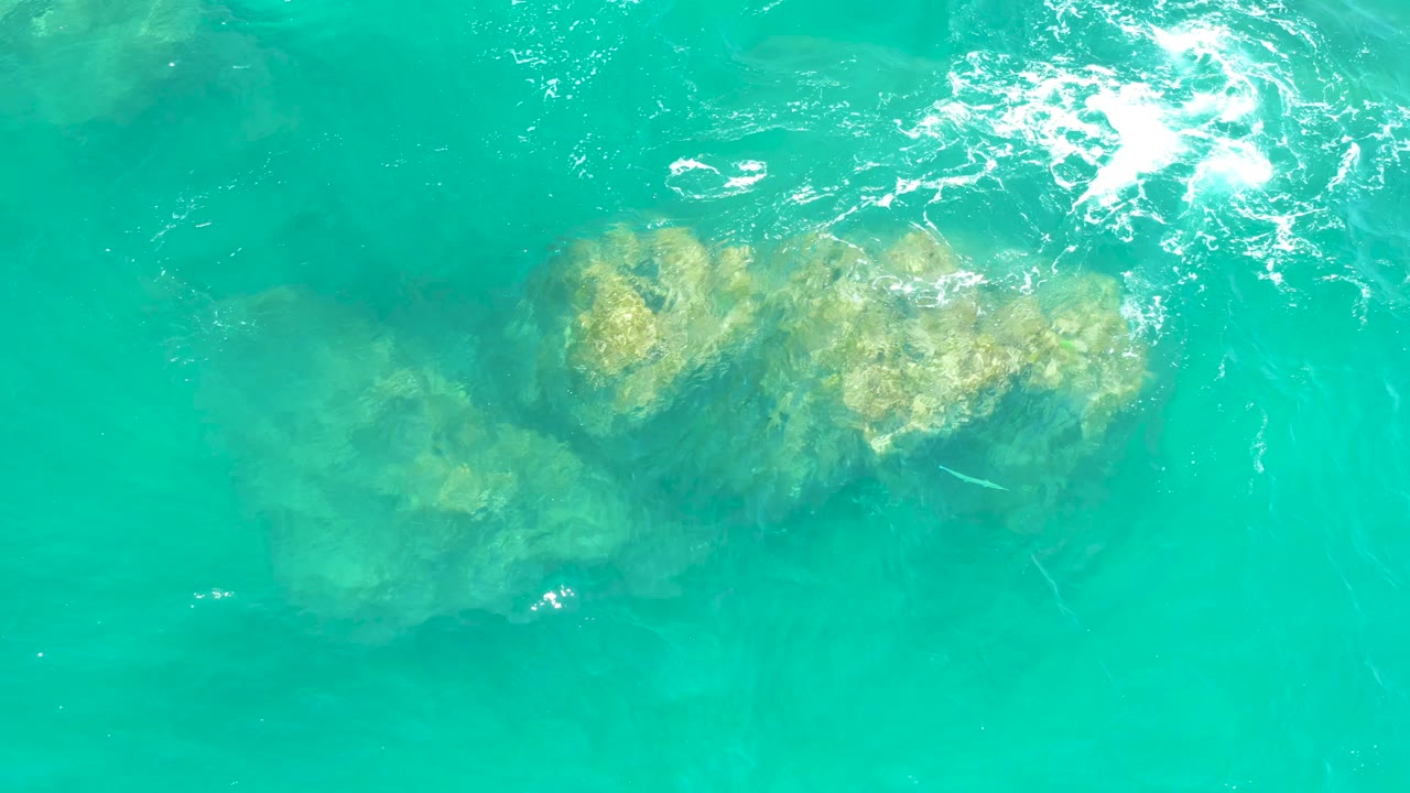 Overhead view at Dreams Los Cabos of clear turquoise water revealing submerged rocks beneath bright surface reflections, with no visible people.