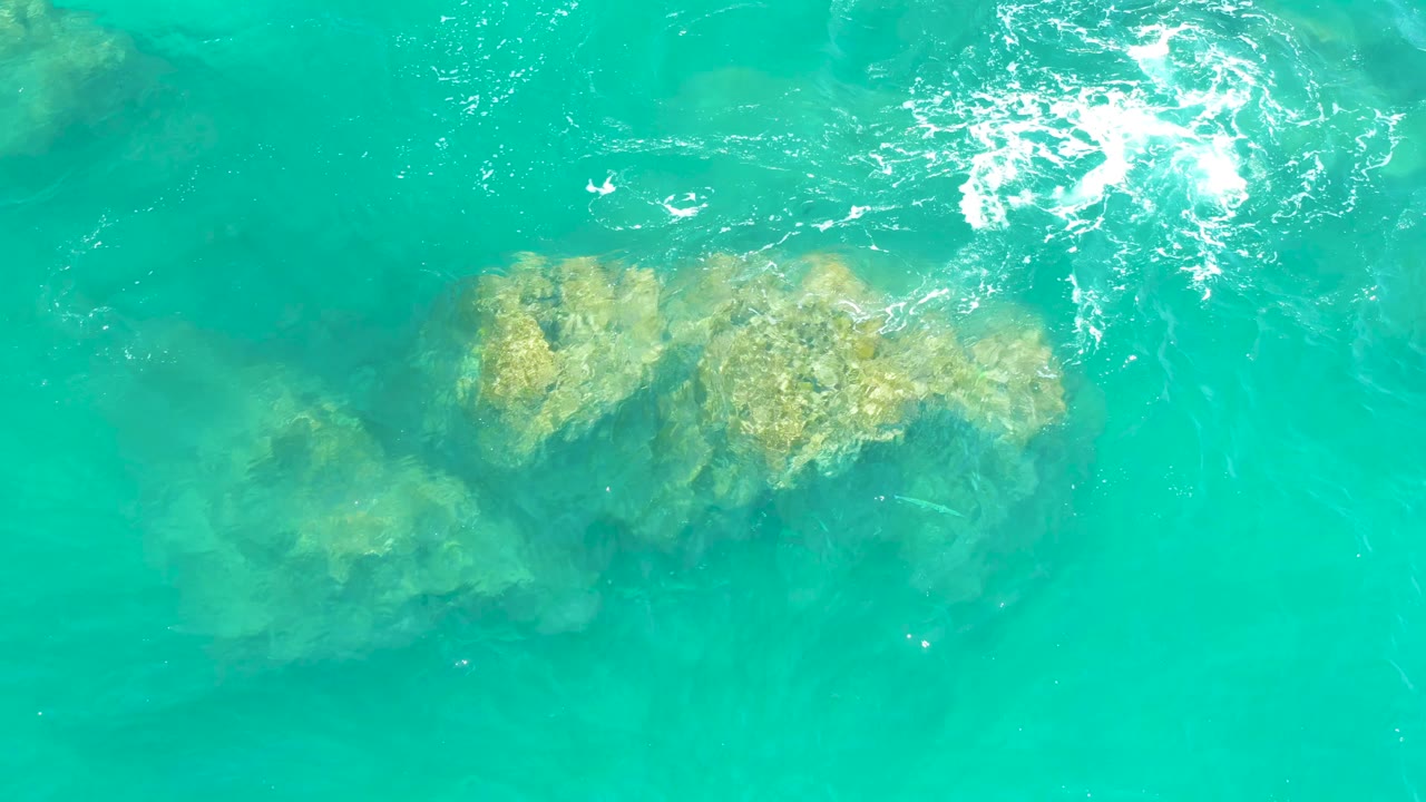 Overhead Dreams Los Cabos water detail with submerged rocks lower in the frame and a band of white surface ripples near the top, with no visible people.