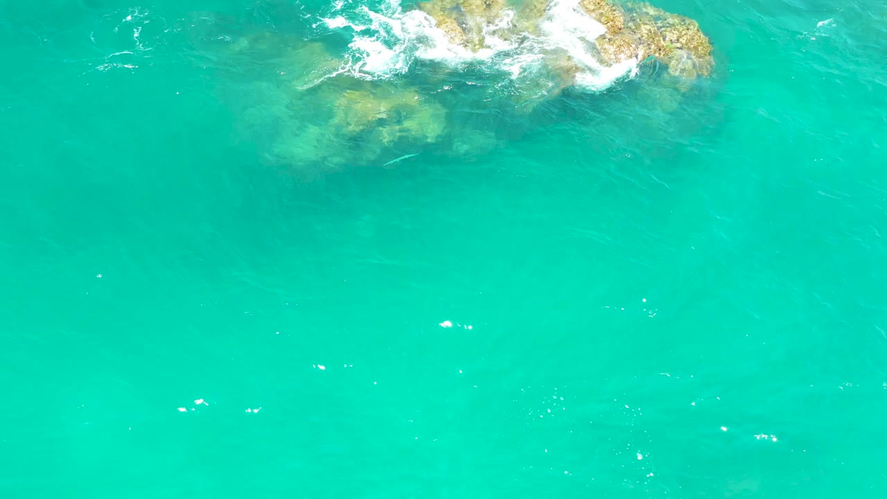 Turquoise water with a rocky outcrop and white foam near the top edge.