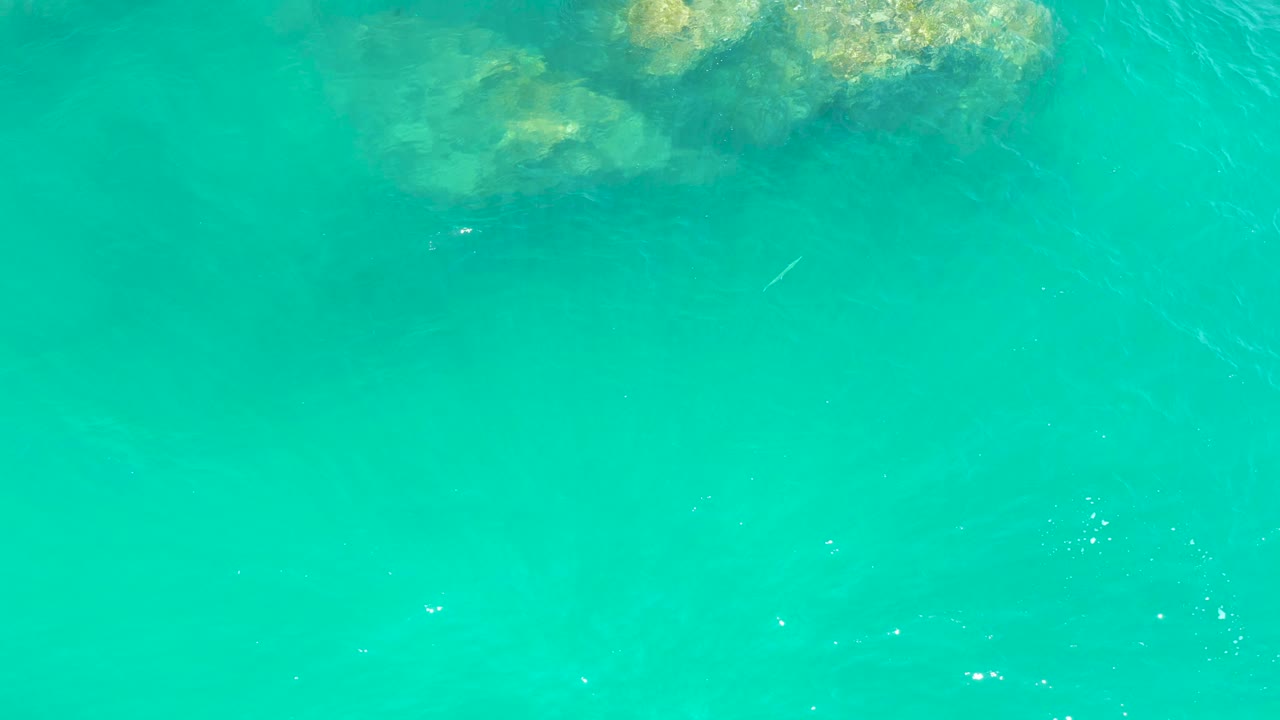 Top-down view of turquoise water at Dreams Los Cabos with submerged rocks along the upper edge and no visible people.