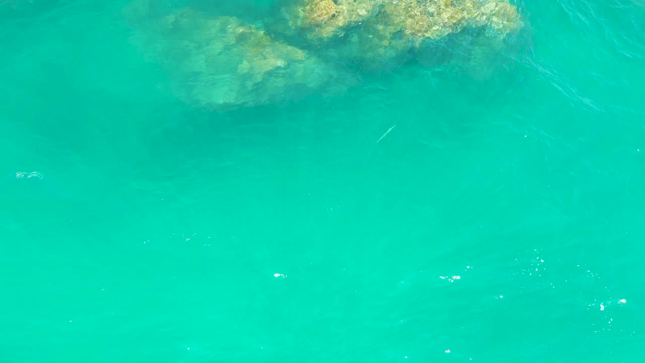 Overhead view of open turquoise water at Dreams Los Cabos, with submerged rocks partly entering from the upper edge and no visible people.