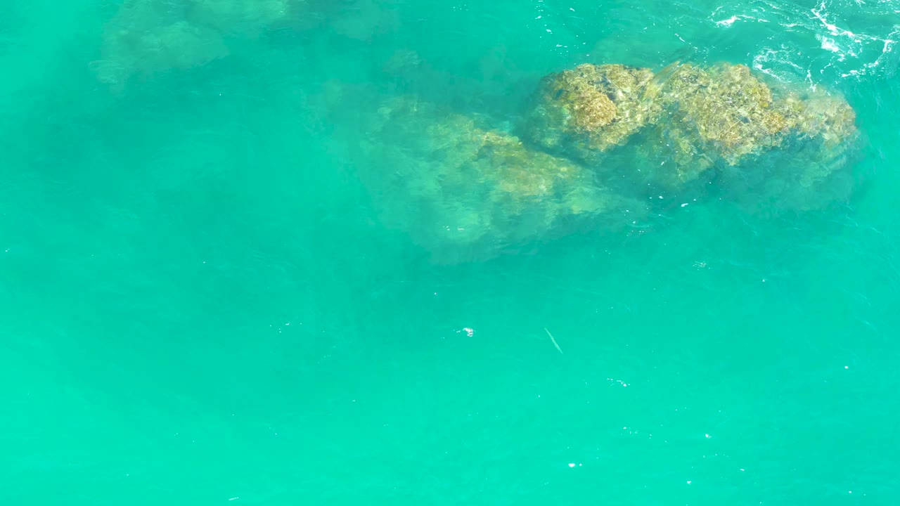 Submerged rocks sit near the top of a turquoise ocean frame at Dreams Los Cabos, with faint ripples shifting across the surface and no visible people.